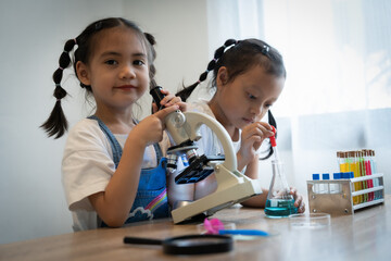Two young girls are looking through a microscope. One of the girls is wearing a blue apron