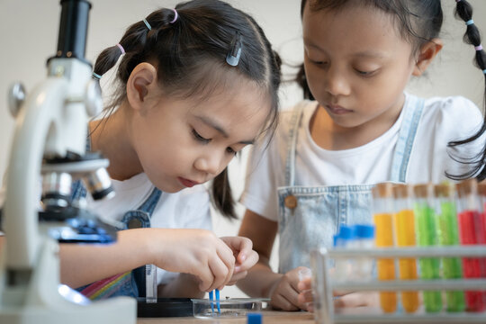 Two young girls are looking at a microscope and a table full of colorful liquids. They seem to be interested in the liquids and the microscope - Powered by Adobe