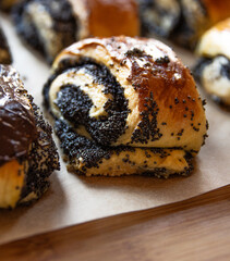 Closeup of freshly baked homemade poppy seed rolls with chocolate topping on parchment paper. Indulgent bakery treats and concerns about unhealthy, fattening diet. Blurred bokeh background.