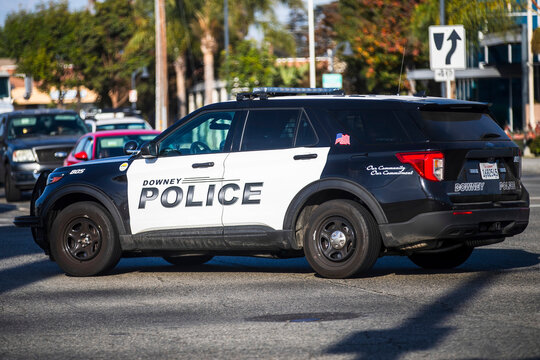 A black and white Downey Police SUV in motion, with buildings blurred in the background.