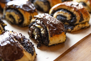 Closeup of freshly baked homemade poppy seed rolls with chocolate topping on parchment paper. Indulgent bakery treats and concerns about unhealthy, fattening diet. Blurred bokeh background.
