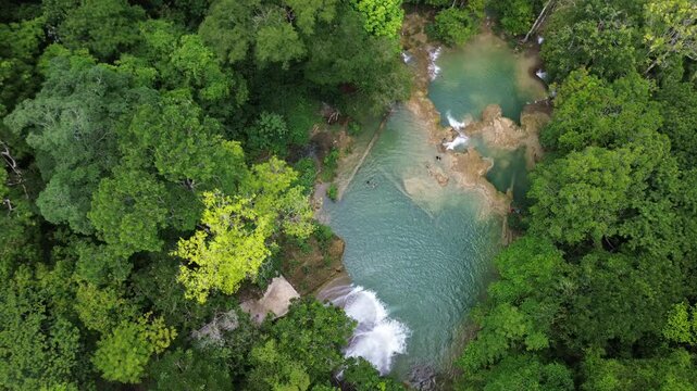 Turquoise waterfalls flowing in dense jungle at Roberto Barrios, aerial perspective descends on people swimming