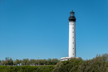 Imponente farol branco com c&uacute;pula preta sobre uma plataforma rochosa &agrave; beira-Mar