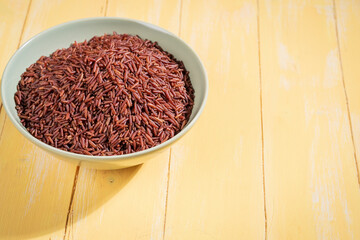 A bowl of red raw rice is placed on a yellow wooden table
