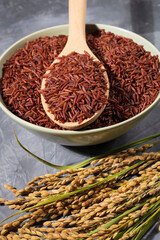 awesome red rice in a bowl with spoon and ears of rice on wood
