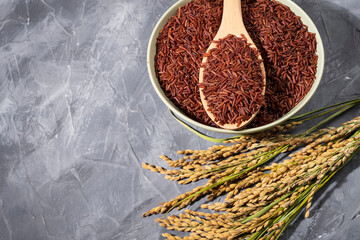 awesome red-rice in a bowl with spoon and ears of rice on wood