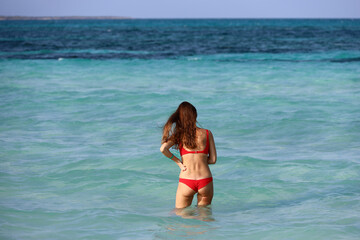 Fototapeta premium Tanned slim woman in red swimsuit standing in sea water, vacation on tropical beach