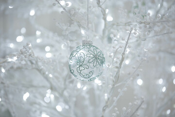 Background delicate glass bauble intricate green floral patterns hangs on white branch glowing bokeh lights. This dreamy and festive background is perfect for holiday and seasonal designs