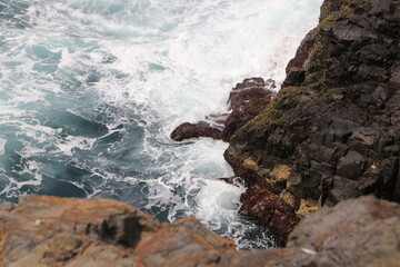A dramatic close-up of ocean waves crashing against rugged, jagged rocks, highlighting the raw power and untamed beauty of nature's force at the water's edge