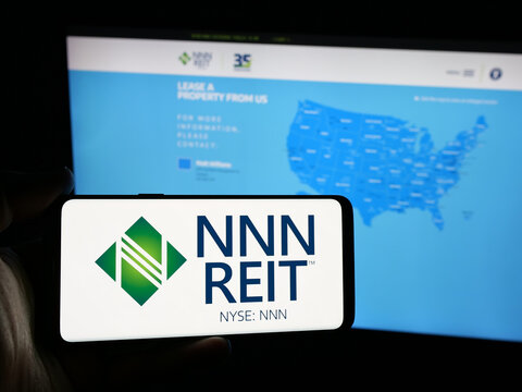 Stuttgart, Germany - 12-09-2024: Person holding smartphone with logo of US real estate company NNN REIT Inc. on screen in front of website. Focus on phone display.