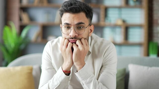 Lonely sad young adult male is bored sitting on sofa in living room at home looking at camera. Tired pensive handsome bearded man is depressed and in a bad mood. Thoughtful guy has problems. Close up