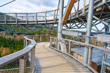Obraz premium Visitors enjoy a leisurely stroll along the elevated wooden walkway of the Sky Walk Tower, offering breathtaking views of the Jizera Mountains and surrounding lush forests.