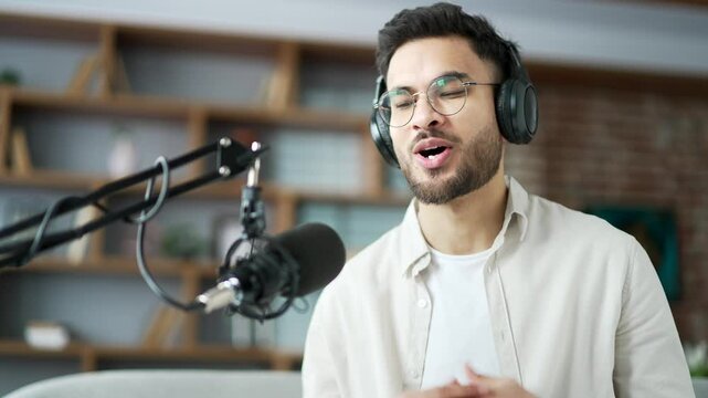 Confident man recording podcast using laptop and microphone sitting in home office. Male in headphones vlogger conducts online broadcast interview or webinar, speaks remotely via video call. Close up