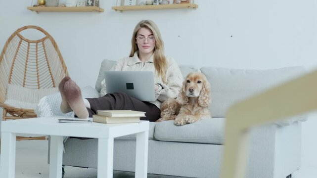 Young Freelance Woman Working on Laptop Sitting at Home with Her Dog