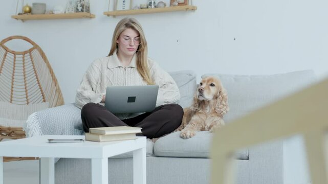 Young Freelance Woman Working on Laptop Sitting at Home with Her Dog