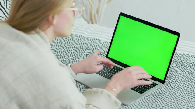 Young Woman In Glasses Using Green Screen Laptop While Lying at Home on Couch. Close up Laptop with Green Mock-up Screen
