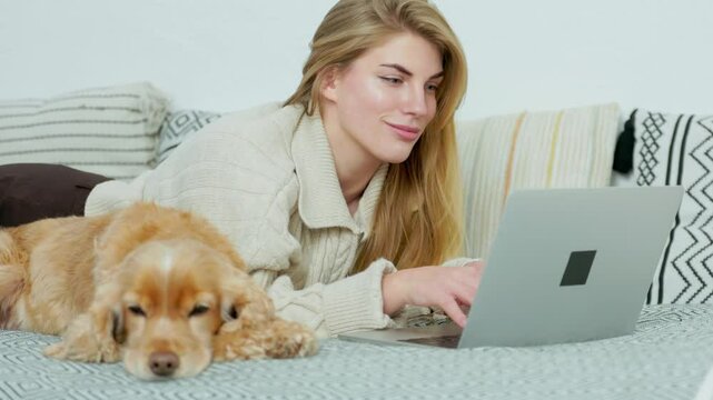 Young Woman Lying on Couch with Her Pet Dog and Using Laptop. Freelancer or Student Girl Works and Studies at Home Online from Laptop