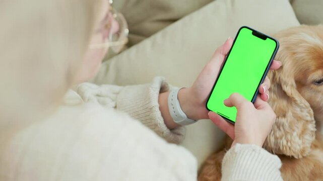 Young Woman Using Green Mock Up Screen Smartphone While Sitting With Her Pet Dog In Cozy Home Room