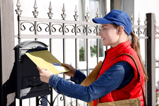 Postwoman putting envelope into mail box outdoors