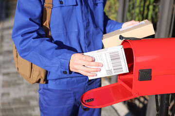 Postman putting parcel into mail box outdoors, closeup