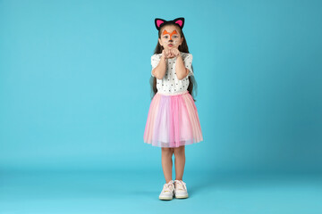 Cute girl with painted face and ears as cat on light blue background