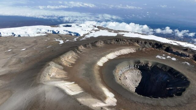 Drone shot of Uhuru Peak on Mount Kilimanjaro with the volcanic crater below. Slowly panning aerial shot
