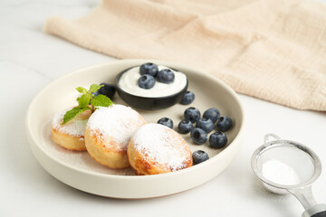 Healthy breakfast, homemade cottage cheese fritters served with fruits and sour cream on bright background.