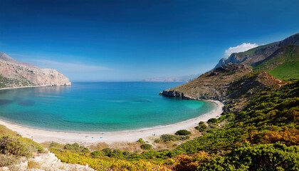 Obraz premium A spectacular crescent-shaped bay with turquoise waters and white sandy beach is framed by dramatic coastal cliffs and green hillsides under a deep blue sky.