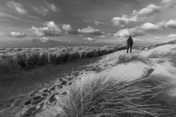 A hiker in the North Holland dunes gazes out over the beach and the North Sea. Footprints in the sand reveal the path taken by the hiker, who stands atop the dunes overlooking the horizon.
