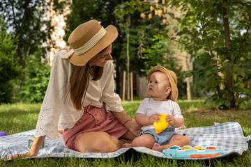 Mother and child in the park looking into each other. Mom and her kid wearing hat while seating on...