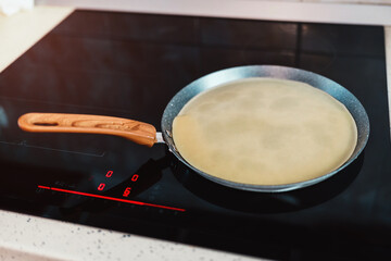 Cooking Crepe Batter on a Nonstick Pan with Wooden Handle on a Modern Induction Stove