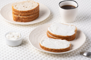 Freshly spread cream cheese on slices of bread served with coffee for a cozy breakfast experience