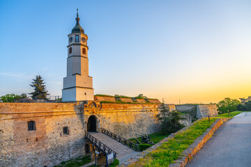 Fototapeta premium As the sun sets over Belgrade, the Clock Tower and Clock Gate at Kalemegdan Fortress illuminate the historic site, highlighting its ancient architecture and serene surroundings.