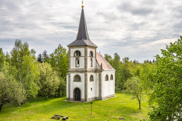 The Church of Saint John of Nepomuk stands proudly on Zvicina Hill, surrounded by lush greenery. Its distinct architecture is a highlight against the backdrop of a cloudy sky in Czechia.