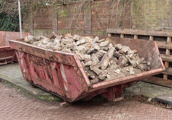 red-colored open steel industrial waste container filled with stone waste
