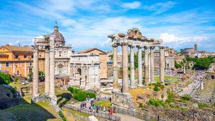 Visitors admire the ancient ruins of the Saturn Temple in the Roman Forum, surrounded by historical...