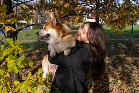 Happy young woman carrying corgi dog in autumn park