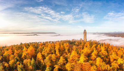 The National Wallace Monument on Abbey Craig surrounded by autumn trees and morning fog in Stirlingshire, Scotland.