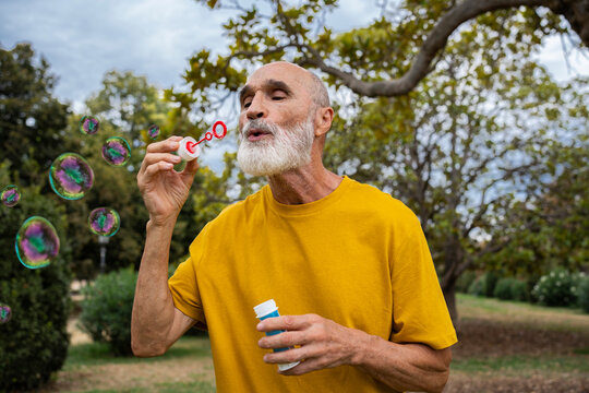 Senior man blowing bubbles with wand in park