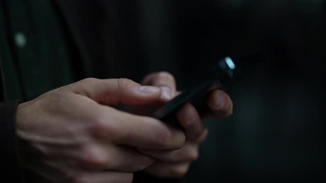 Close-up of male hands scrolling and swiping on smartphone screen while standing on urban street at evening. Close of young man browsing internet, checking social media, using mobile application.