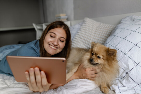 Smiling woman using tablet PC lying down with dog on bed at home