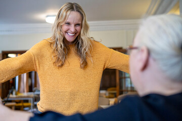 Excited caregiver with arms outstretched looking at senior woman at retirement community