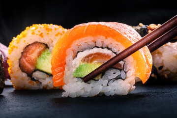 Sushi rolls on a black background. Uramaki with salmon, avocado, and cream cheese, and other rolls, with chopsticks
