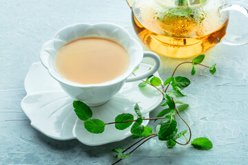 Mint tea. A cup of peppermint tea with fresh mint leaves and a tea pot, on a blue background