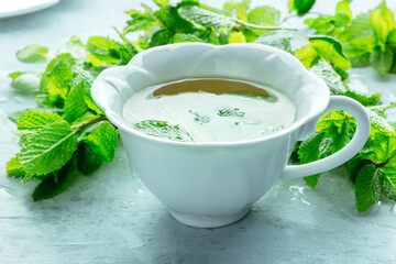 Mint tea. A cup of peppermint tea with fresh mint leaves, on a blue background