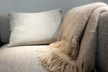Close-up of warm beige blanket cast on the armrest of a gray sofa with a cushion illuminated for a...