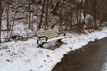 A bench in a winter park surrounded by snow, located on a snowy trail with melting snow.