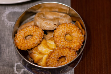 Tin of cookies with a variety of shapes and sizes. The tin is on a table. The cookies are arranged in a way that they look like they are ready to be eaten