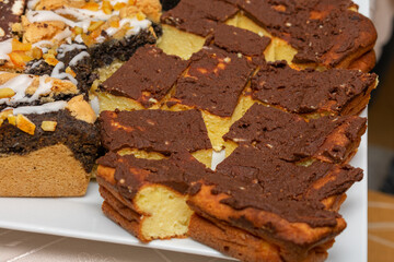 Plate of desserts with a piece of chocolate cake on top. The cake is covered in chocolate and has a white frosting. There are also other desserts on the plate, including a piece of cake with nuts