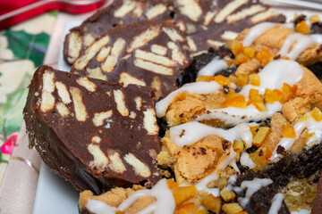 Plate of desserts with a piece of chocolate cake on top. The cake is covered in chocolate and has a white frosting. There are also other desserts on the plate, including a piece of cake with nuts